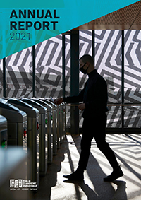 The 2021 Annual Report cover shows a person walking through myki turnstiles, tapping on their myki card. The person is silhouetted by light from windows behind them, but their facemask is visible. there is a striped pattern on the window behind them.
