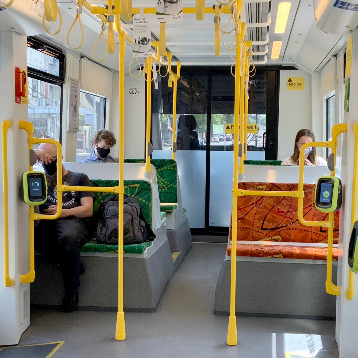 Image shows three people wearing face masks and employing social distancing while travelling on a tram.