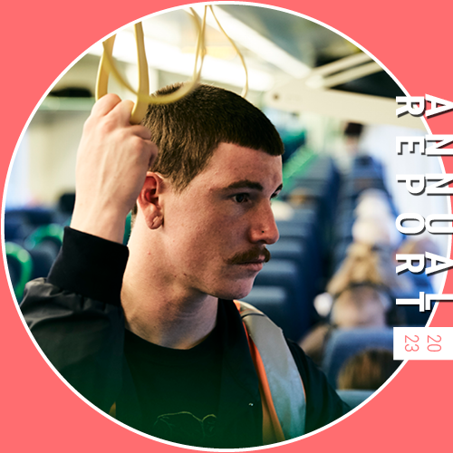 Image shows a caucasian man travelling on a train. He is holding a yellow ceiling-mounted hand loop. He has closely-cropped brown hair and a moustache and is looking away from the camera. The words 'annual report 2023' appear on the right of the image.