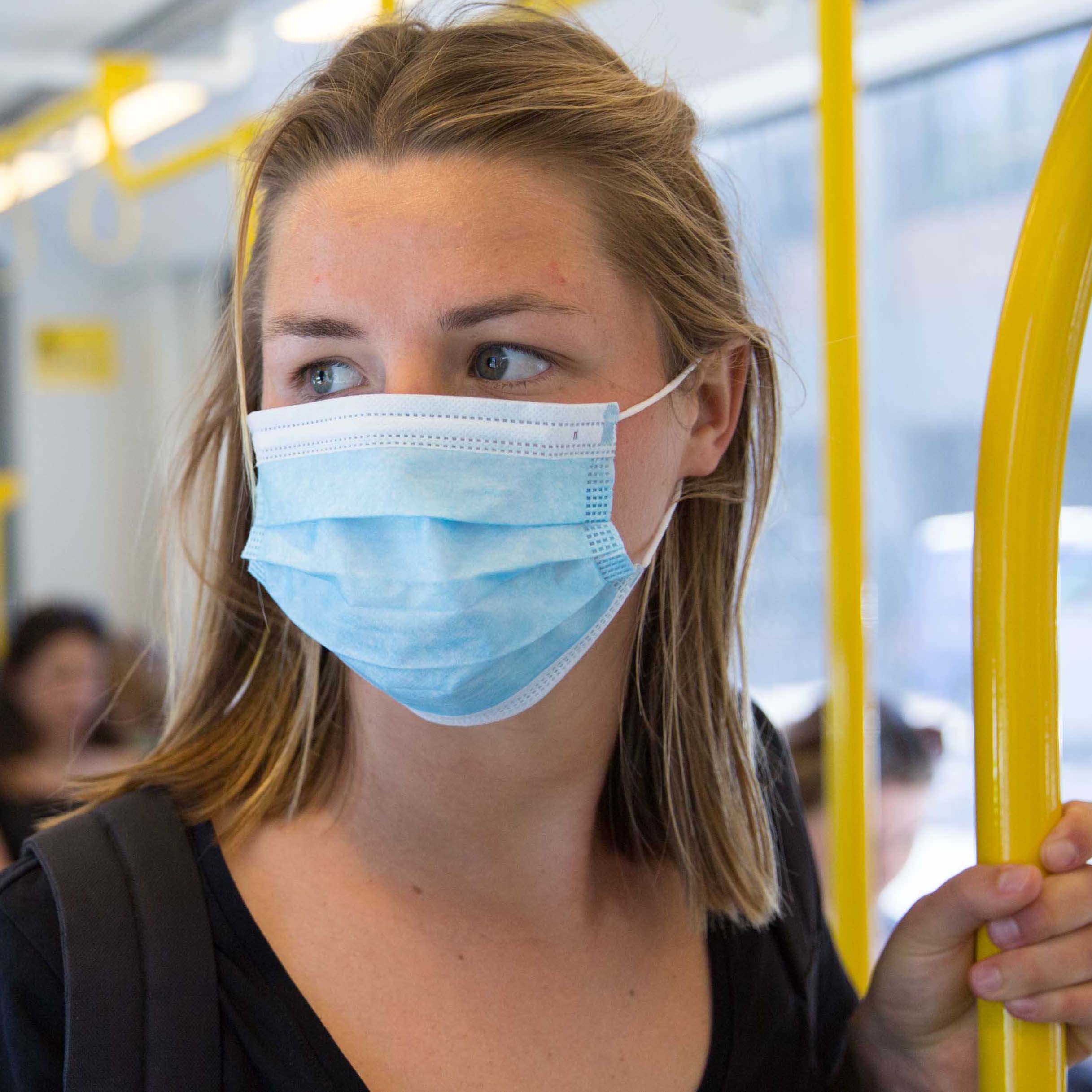 Image shows a woman on a tram wearing a surgical face mask during the COVID-19 pandemic.