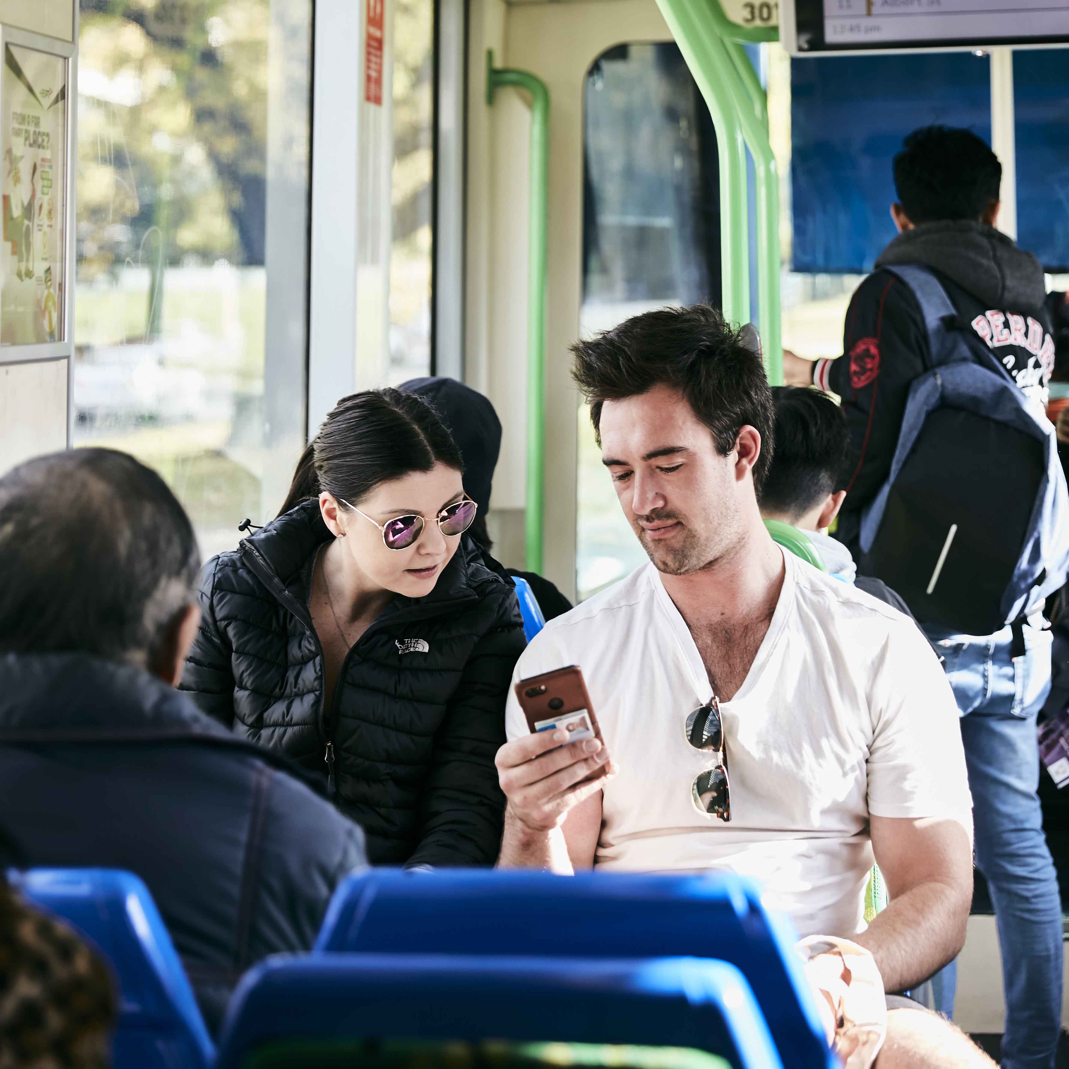 Image shows two people looking at a mobile phone while travelling on a tram.