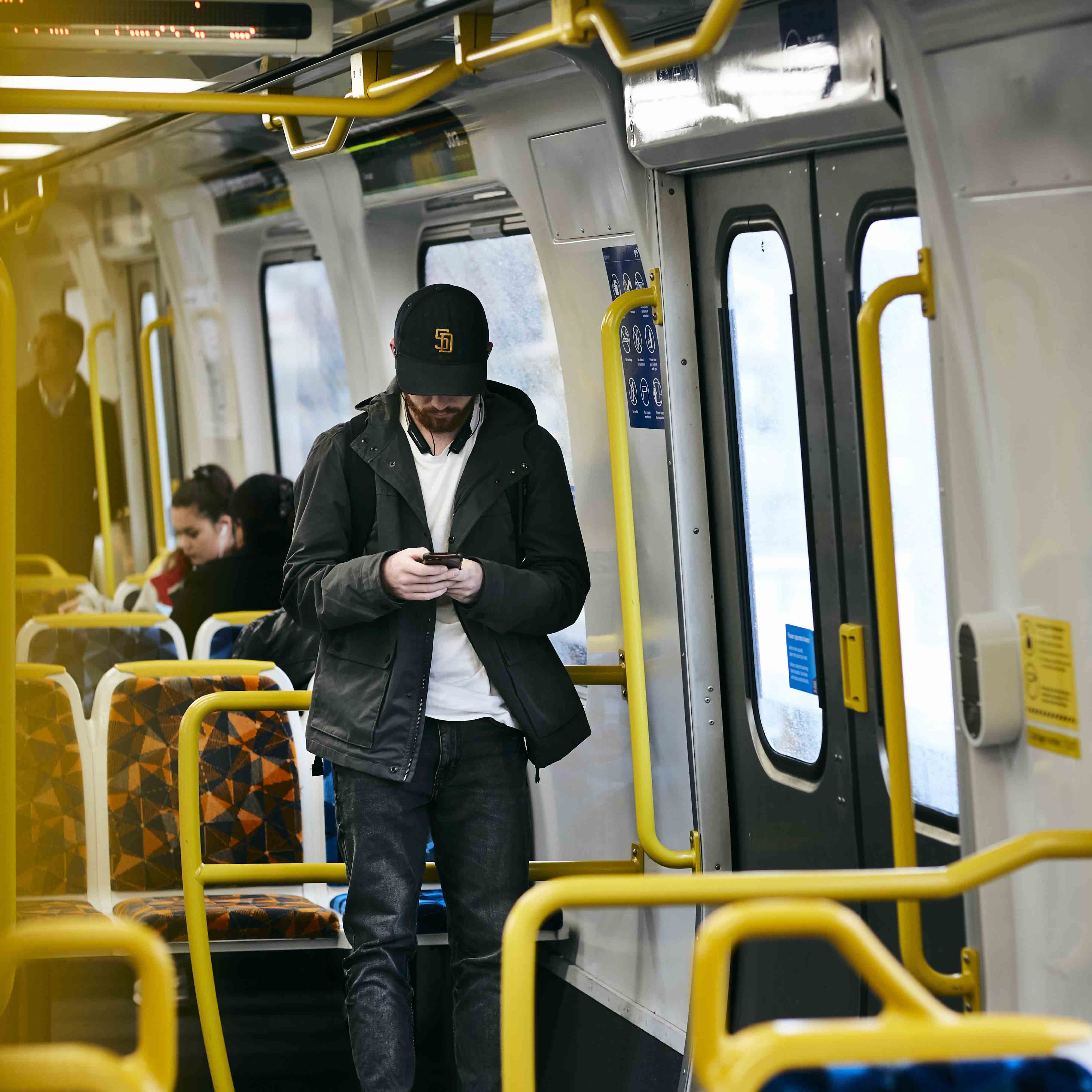 Image shows a man looking at his phone while travelling on a Metro train.