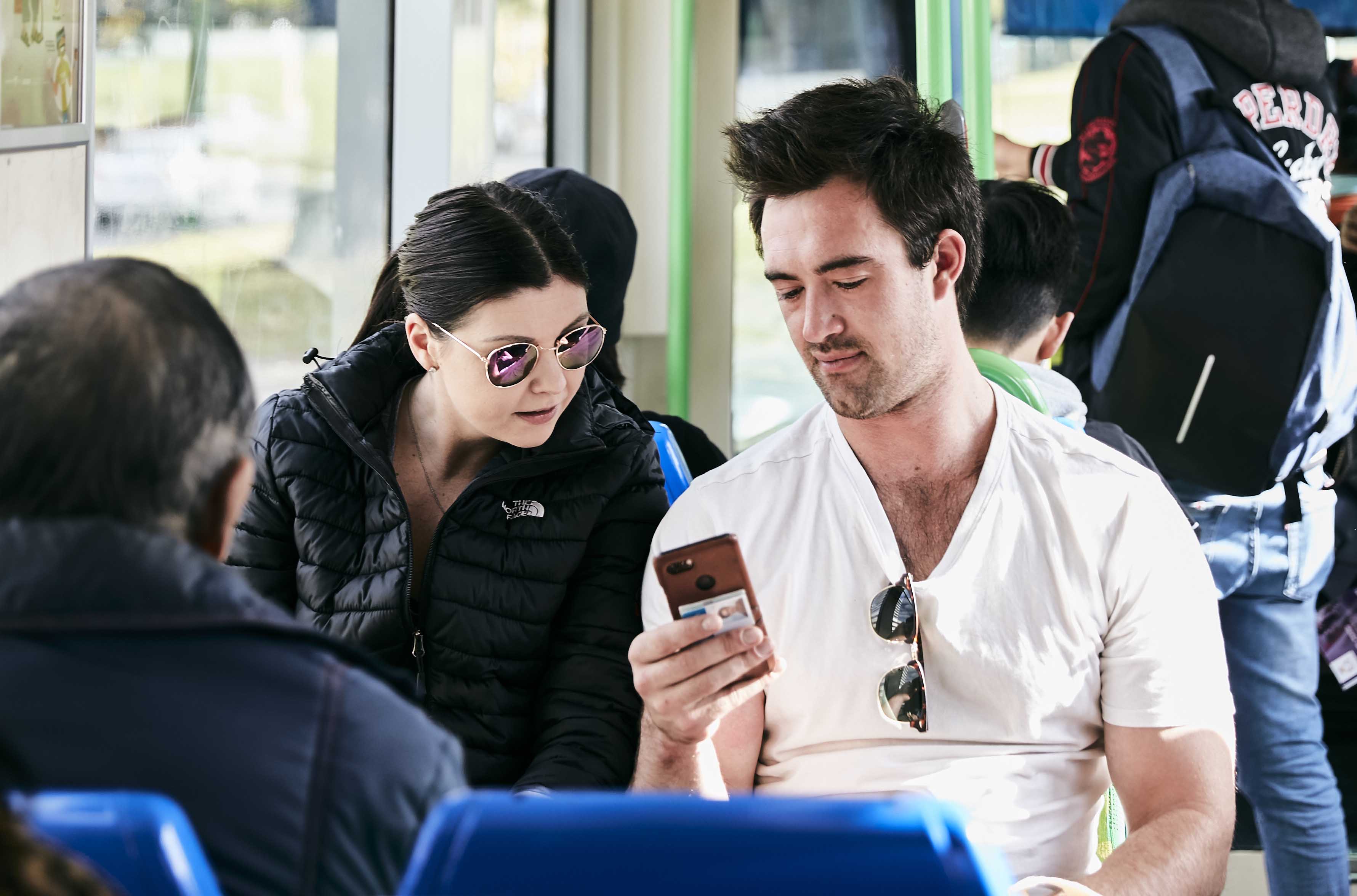 Image shows two people looking at a mobile phone while travelling on a tram.