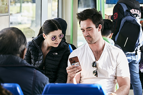 Image shows two people looking at a mobile phone while travelling on a tram.