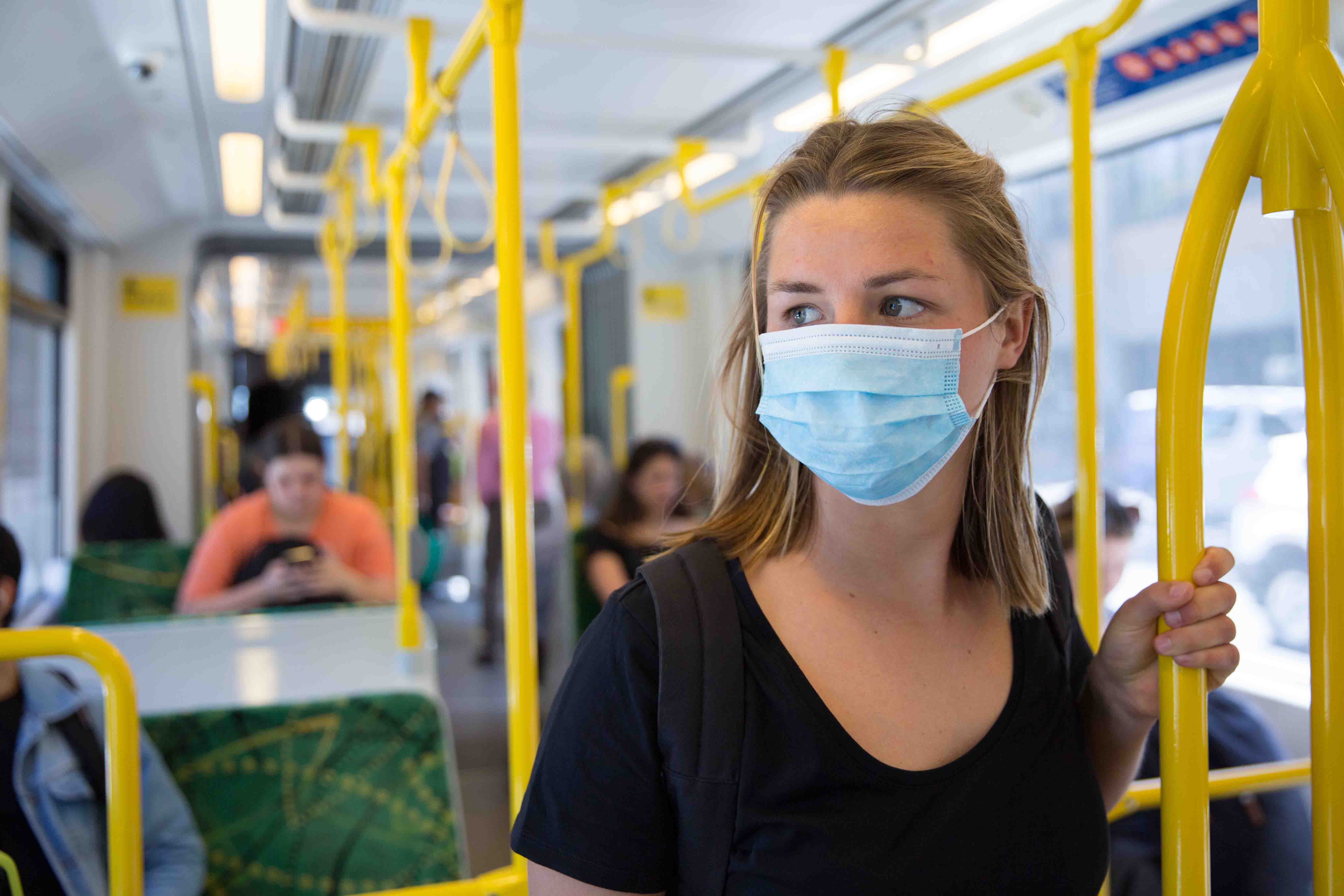 Image shows a woman on a tram wearing a surgical face mask during the COVID-19 pandemic.