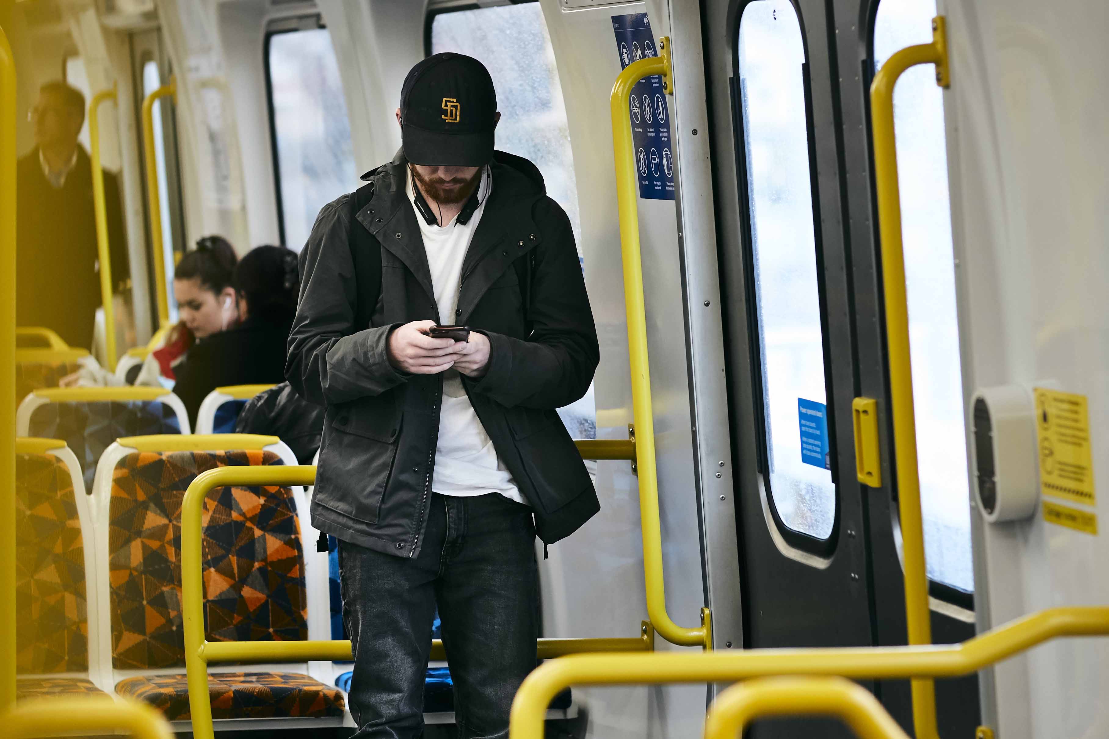 Image shows a man looking at his phone while travelling on a Metro train.